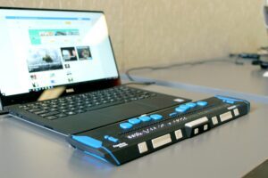 A laptop connected to a braille display, symbolizing gaining expertise in testing digital content using assistive technologies like keyboard navigation and screen readers.